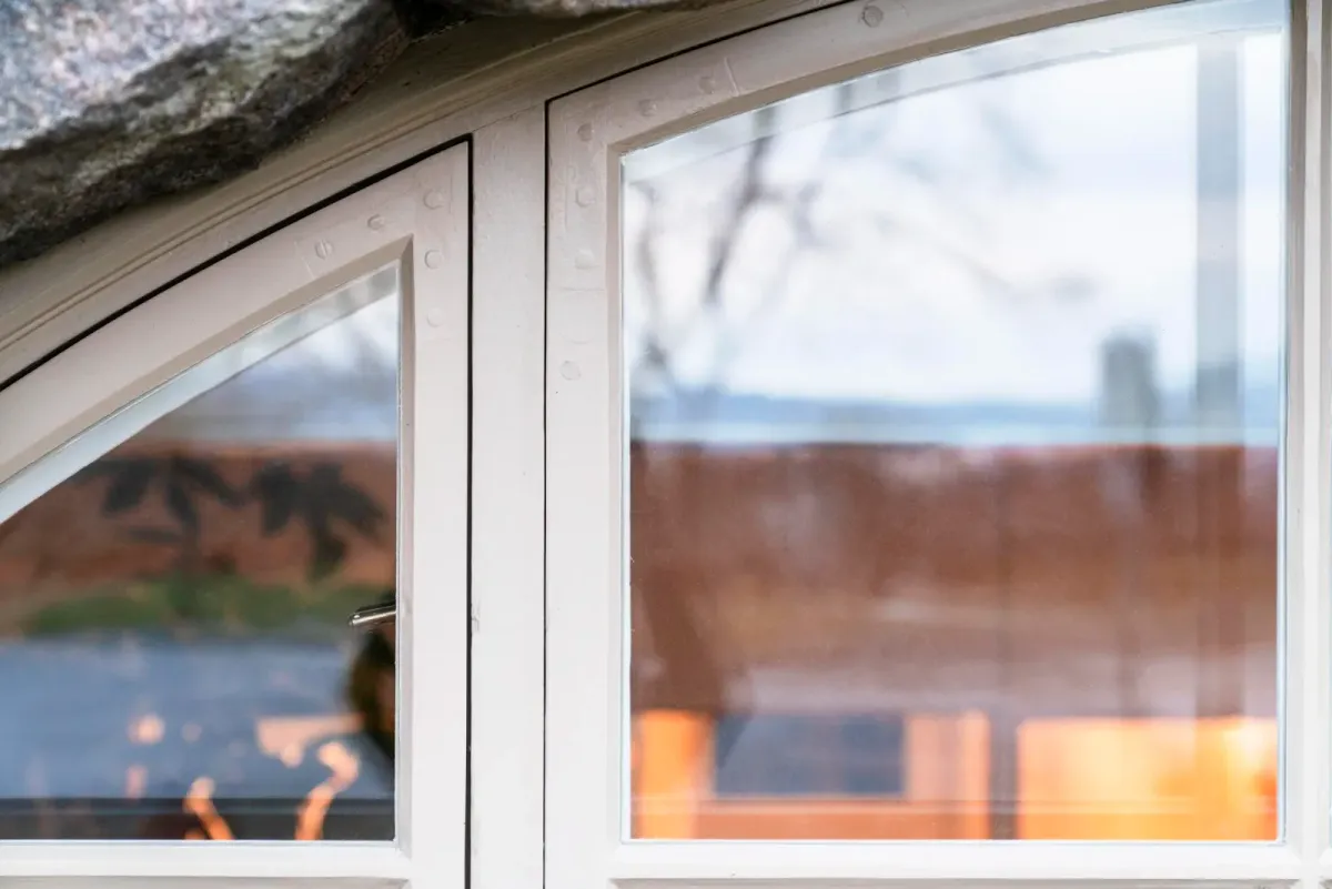Detalj av et restaurert buevindu med hvit ramme innfelt i en grovhugget granittfasade. – bilde 2