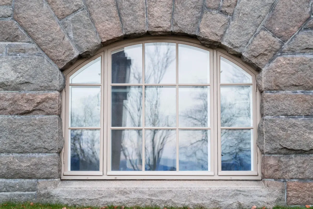 Detalj av et restaurert buevindu med hvit ramme innfelt i en grovhugget granittfasade. – bilde 4